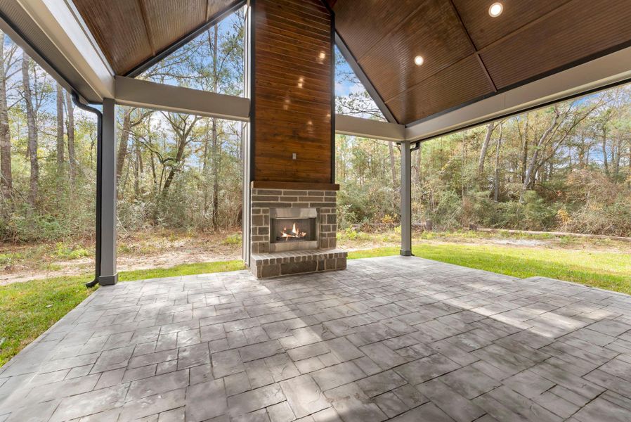 This outdoor space features a covered patio with a vaulted ceiling, built-in lighting, and a cozy fireplace. It opens to a lush, wooded backdrop, providing a serene and private views. Ideal for relaxation or entertaining.