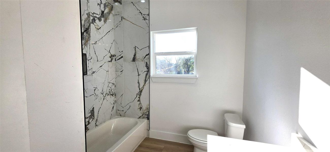 This bathroom features a sleek design with a striking marble-patterned shower wall, a bathtub, and a window for natural light.