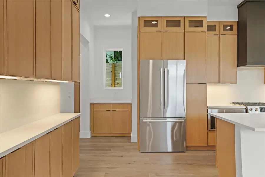 A streamlined kitchen showcasing modern wood cabinetry, white countertops, and a sleek stainless steel refrigerator.