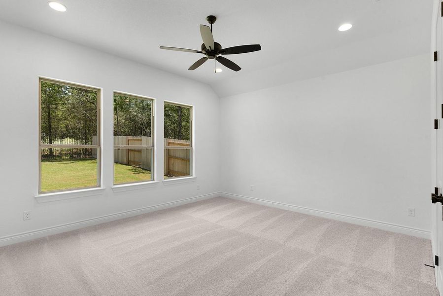 A quiet bedroom retreat with plush carpeting and ample natural illumination from multiple windows overlooking a private yard.
