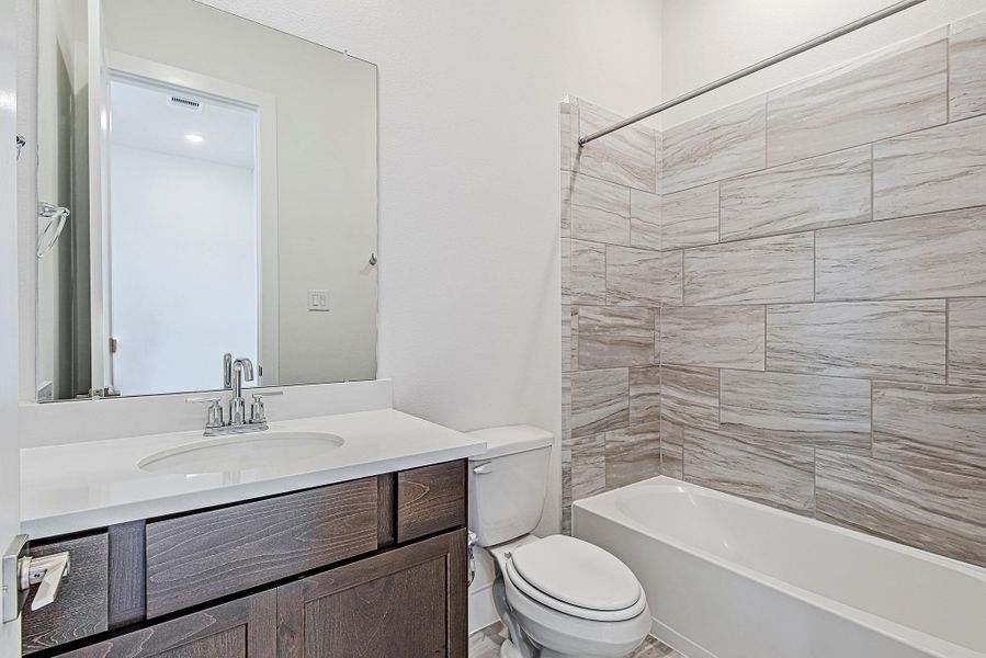 Full bathroom with sleek fixtures and a clean modern aesthetic—featuring a chic tile-surround tub/shower combo and stylish dark cabinetry. Full bathroom with sleek fixtures and a clean modern aesthetic—featuring a chic tile-surround tub/shower combo and stylish dark cabinetry.