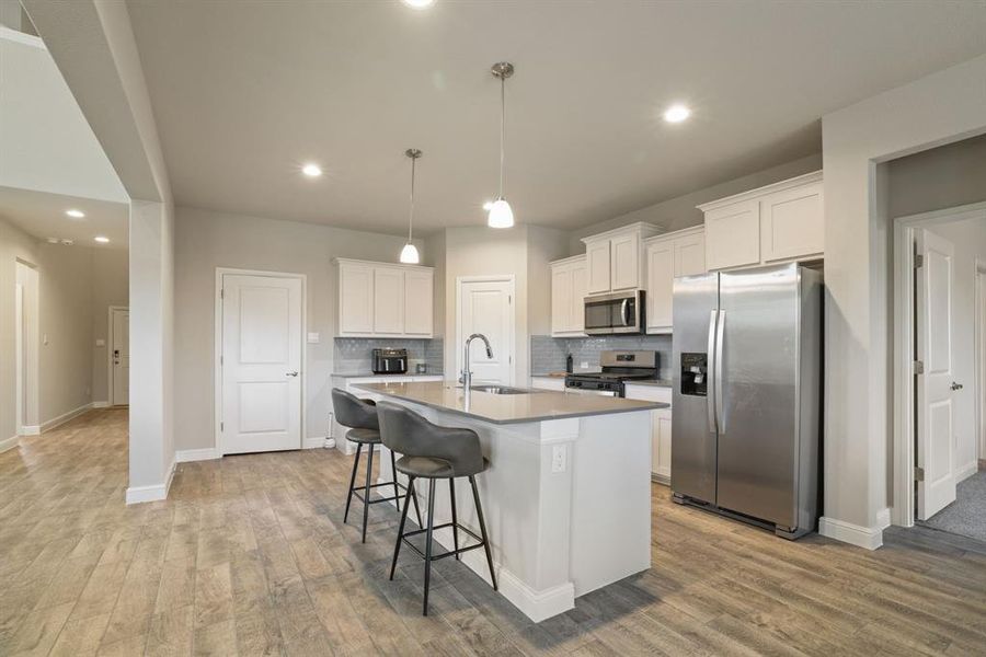 Kitchen featuring stainless steel appliances, white cabinets, a breakfast bar, decorative backsplash, and a kitchen island with sink Kitchen featuring stainless steel appliances, white cabinets, a breakfast bar, decorative backsplash, and a kitchen island with sink