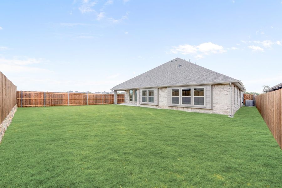Backyard with large green lawn, wood privacy fence, and brick home with gray shingle roof