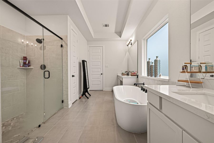 The spa inspired primary bathroom features dual vanities, a soaking tub, and a frameless glass shower. The spa inspired primary bathroom features dual vanities, a soaking tub, and a frameless glass shower.
