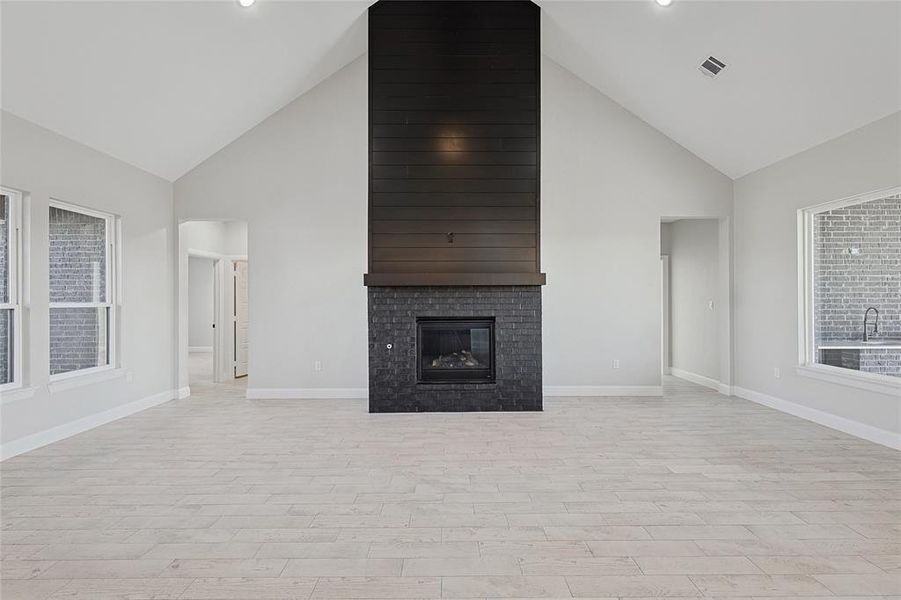 Unfurnished living room with light hardwood / wood-style flooring, high vaulted ceiling, and a brick fireplace