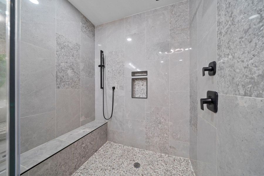 This expansive bathroom features a stunning, oversized walk-in shower encased in seamless glass, complete with designer floor-to-ceiling tiling and a rainfall showerhead.