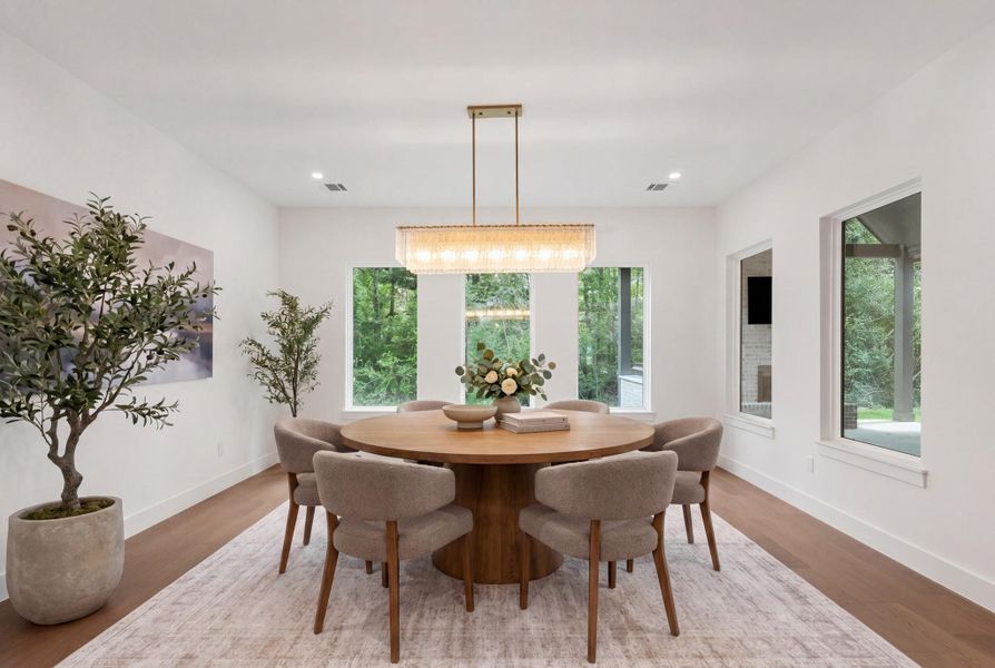 Light-filled dining area surrounded by oversized windows that bring in peaceful backyard views. A statement linear chandelier with textured glass detail anchors the space overhead, adding warmth and character. Glass door access to the covered patio makes it easy to transition outdoors, while the clean white walls and wide-plank wood flooring keep the room bright and refined. Perfectly positioned for everyday meals with a seamless connection to the outdoor living space.