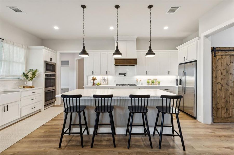 Modern kitchen featuring a large central island, white shaker-style cabinetry, stainless steel appliances, and wood-finish flooring