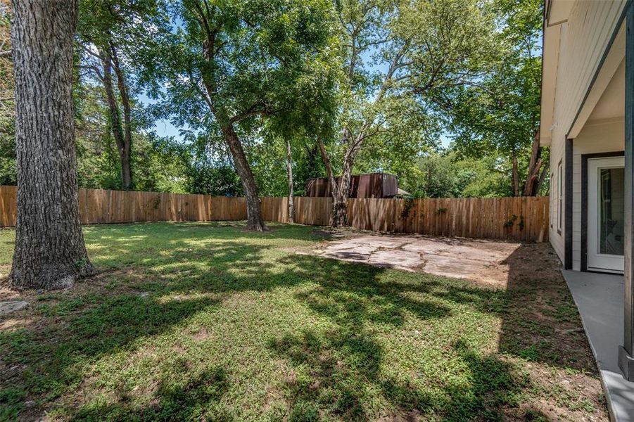 Expansive backyard featuring a privacy fence, mature trees, a concrete patio area, and a concrete pathway alongside the home Expansive backyard featuring a privacy fence, mature trees, a concrete patio area, and a concrete pathway alongside the home