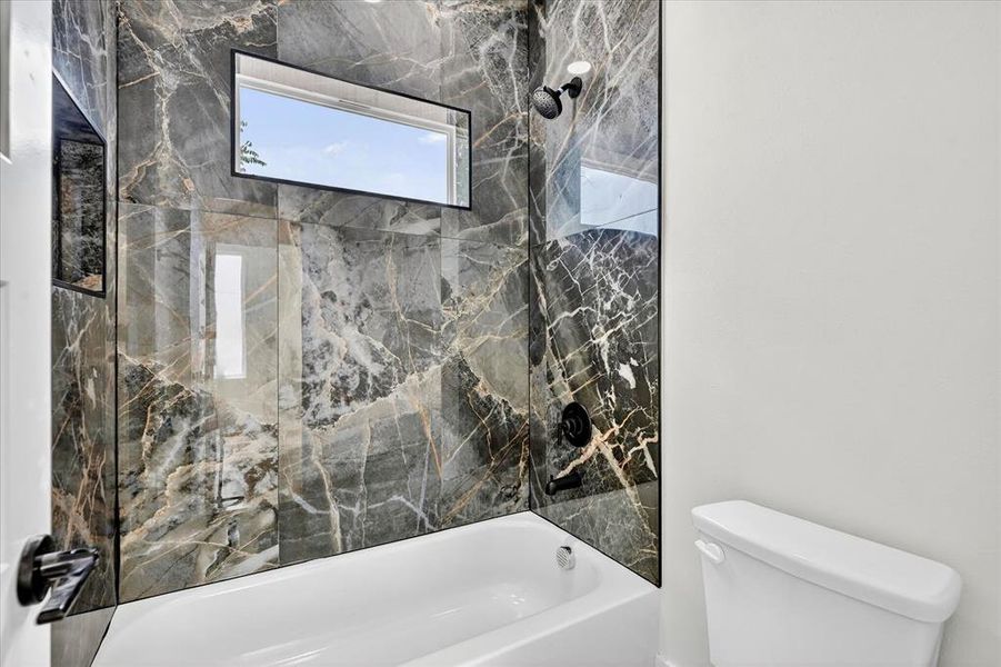 Bathtub and shower combination featuring floor-to-ceiling marbled tile, a built-in window, and matte black fixtures