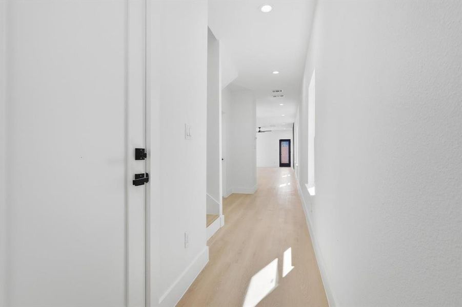 Bright hallway with light wood-finish flooring, recessed lighting, and white walls Bright hallway with light wood-finish flooring, recessed lighting, and white walls