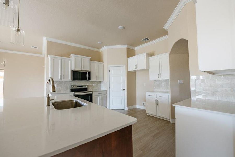 Kitchen featuring white cabinetry, light stone counters, appliances with stainless steel finishes, crown molding, and decorative backsplash Kitchen featuring white cabinetry, light stone counters, appliances with stainless steel finishes, crown molding, and decorative backsplash