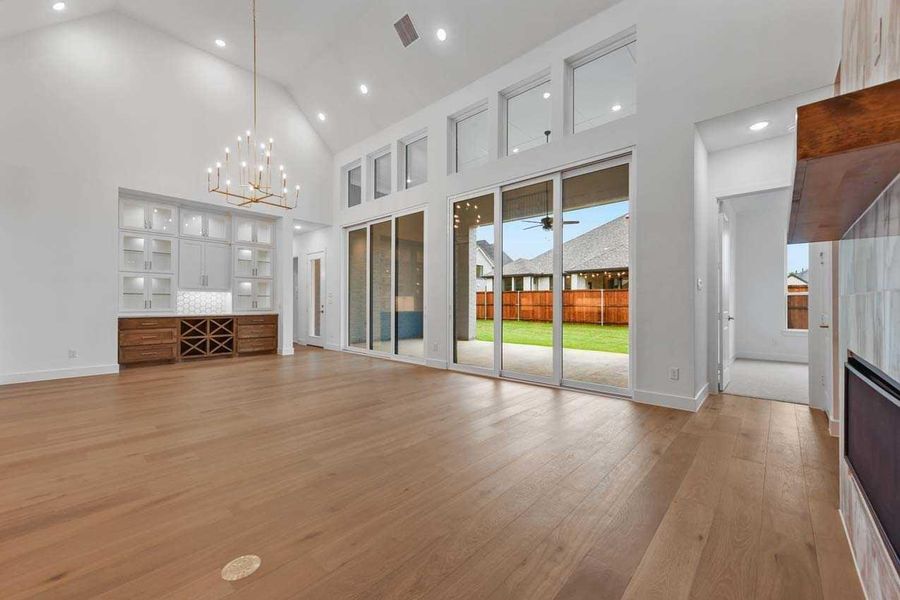 Unfurnished living room with ceiling fan with notable chandelier, light hardwood / wood-style flooring, and a towering ceiling