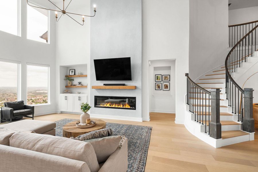 Two-story living area featuring a curved staircase with dark balusters and wood-finish treads, a linear electric fireplace with a wood mantle, and built-in shelving with lower cabinetry Two-story living area featuring a curved staircase with dark balusters and wood-finish treads, a linear electric fireplace with a wood mantle, and built-in shelving with lower cabinetry