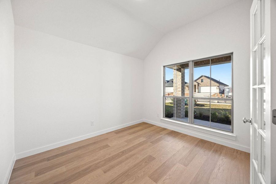 A well-lit room offers vaulted ceilings and rich wood flooring.