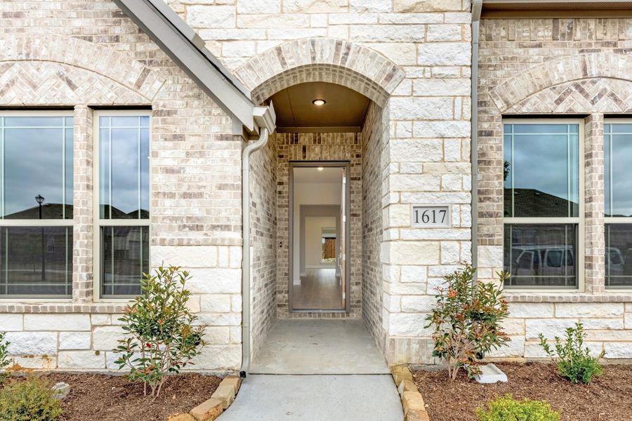 Front entry of home 1617 with arched brick doorway, stone exterior, and small landscaped shrubs on each side