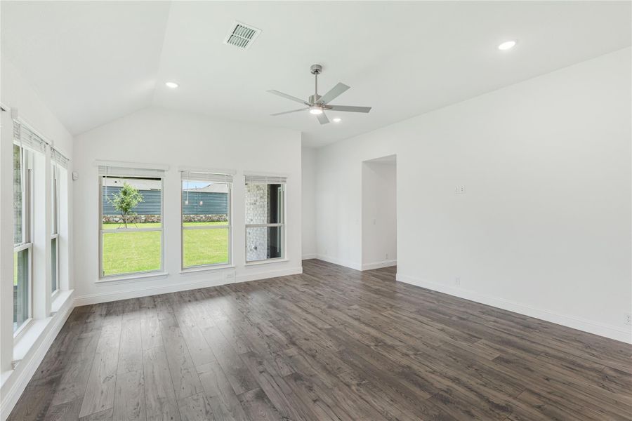 Open living room with vaulted ceiling, ceiling fan, dark hardwood floors, and large windows overlooking backyard Open living room with vaulted ceiling, ceiling fan, dark hardwood floors, and large windows overlooking backyard