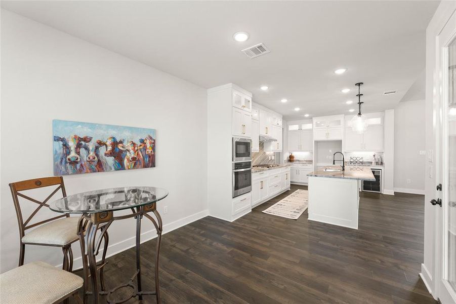 Kitchen with recessed lighting, pendant lighting, a kitchen island with sink, white cabinets, and dark wood-style floors Kitchen with recessed lighting, pendant lighting, a kitchen island with sink, white cabinets, and dark wood-style floors