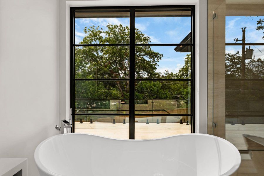 An elegant soaking tub rests before a large window framing serene leafy views.