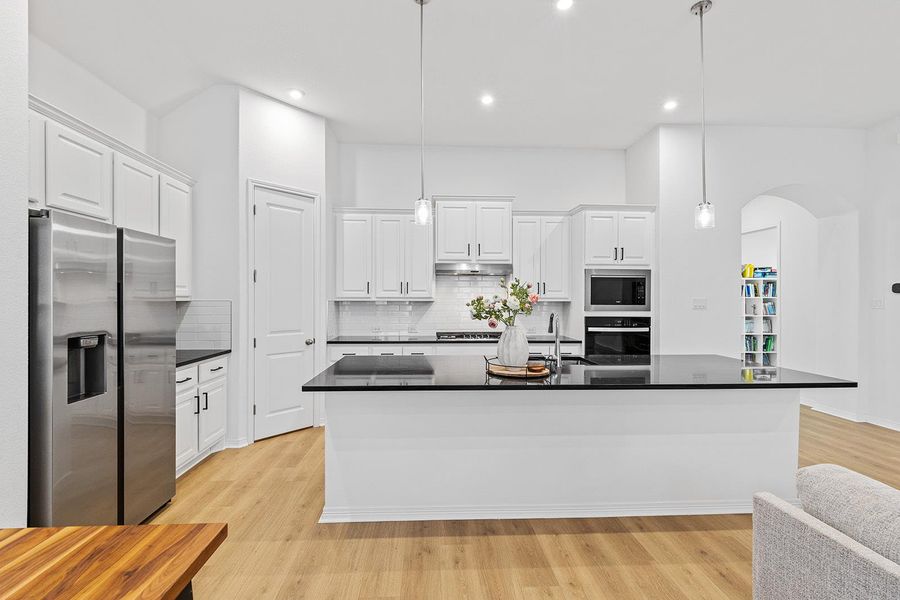 Kitchen featuring decorative backsplash, stainless steel appliances, hanging light fixtures, white cabinets, and recessed lighting