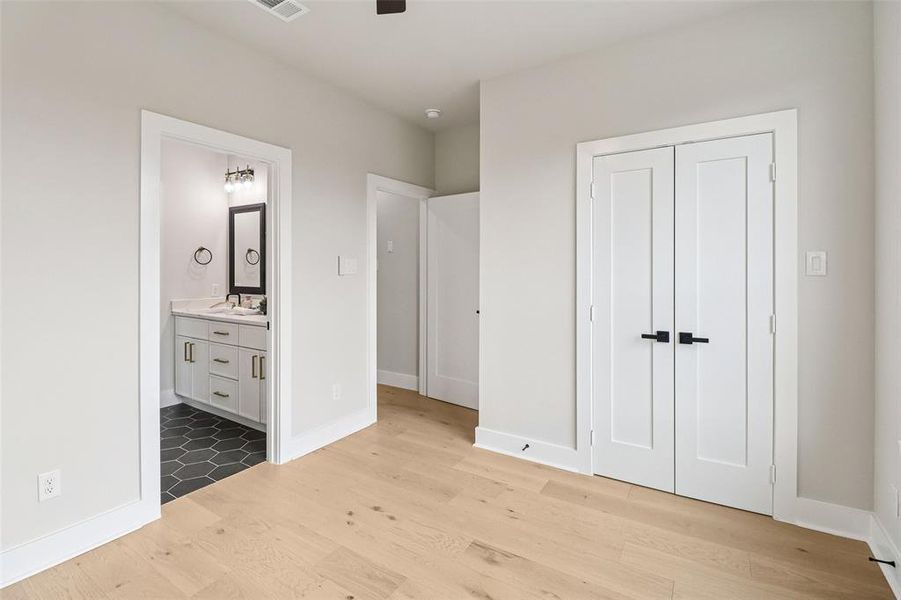 Unfurnished bedroom featuring light wood-style flooring, a closet, a ceiling fan, and ensuite bath