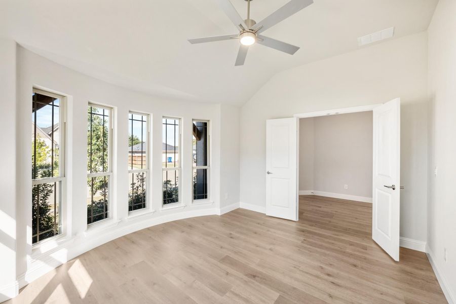 Empty bedroom with vaulted ceiling, ceiling fan, curved bay windows, and light hardwood floors Empty bedroom with vaulted ceiling, ceiling fan, curved bay windows, and light hardwood floors