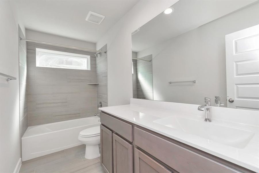 Indulge in refined charm in the secondary bathroom, where the tile flooring harmonizes with a bath/shower combo surrounded by tasteful tile. Wood cabinets, coupled with a gorgeous countertop, elevate the space, cultivating a truly welcoming atmosphere. Sample photo of completed home with similar floor plan. Actual colors and selections may vary.