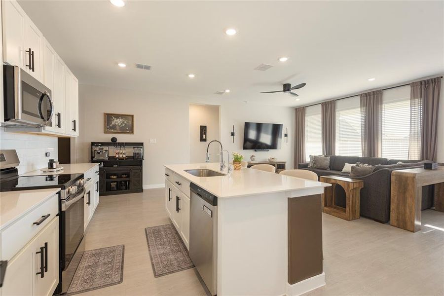 Modern kitchen featuring white cabinetry with black hardware, stainless steel appliances, a center island with sink, and light-colored countertops Modern kitchen featuring white cabinetry with black hardware, stainless steel appliances, a center island with sink, and light-colored countertops
