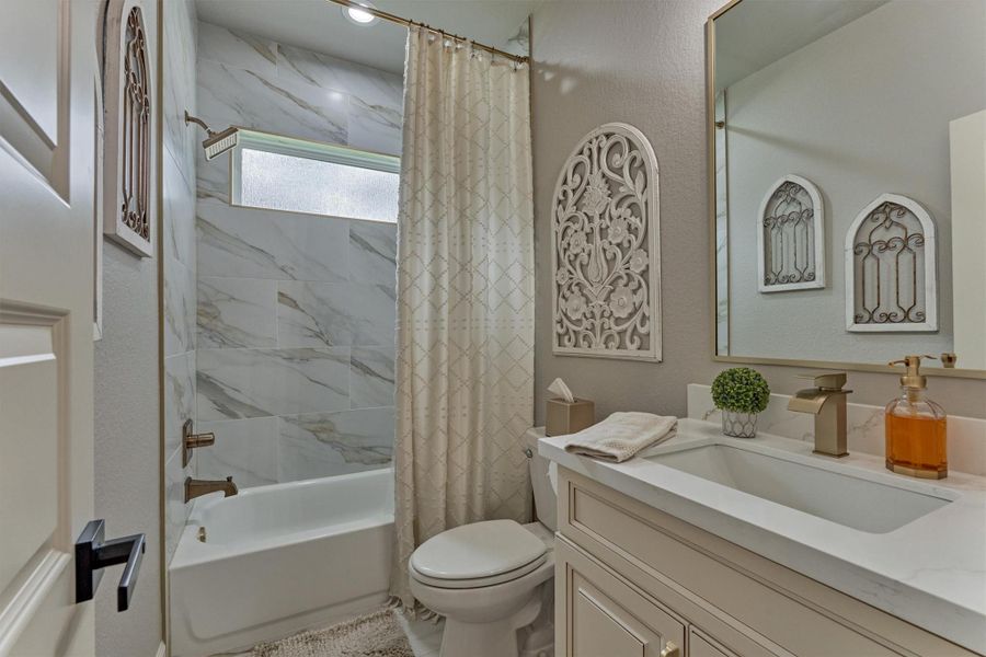 This beautifully appointed bathroom with sleek quartz countertops, upgraded cabinets, a framed mirror, tiled shower bath/tub and sophisticated brushed brass fixtures is located at the front of the house and next to a secondary bedroom. This beautifully appointed bathroom with sleek quartz countertops, upgraded cabinets, a framed mirror, tiled shower bath/tub and sophisticated brushed brass fixtures is located at the front of the house and next to a secondary bedroom.