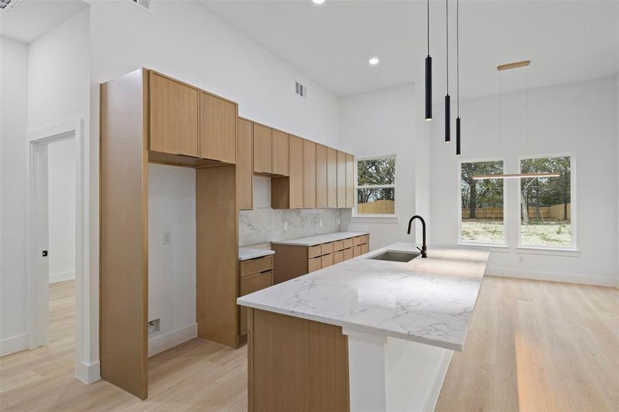 Kitchen featuring light stone countertops, a kitchen island with sink, backsplash, light wood-style flooring, and recessed lighting