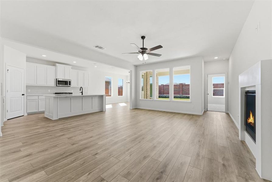 Unfurnished living room with a lit fireplace, recessed lighting, ceiling fan, and light wood-style flooring