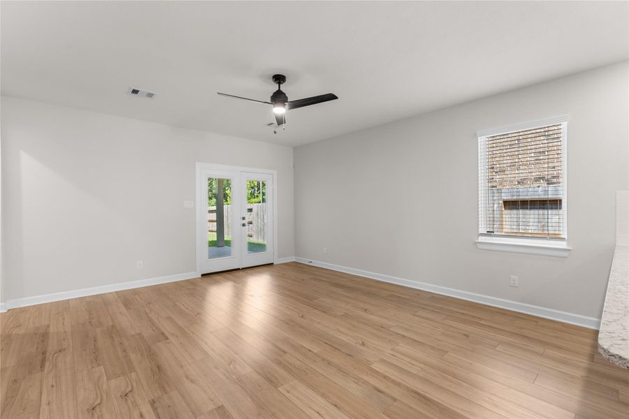 Spacious living room featuring abundant natural light, wood-look flooring, and French doors leading to the covered patio. Enjoy peaceful backyard views with no rear neighbors Spacious living room featuring abundant natural light, wood-look flooring, and French doors leading to the covered patio. Enjoy peaceful backyard views with no rear neighbors