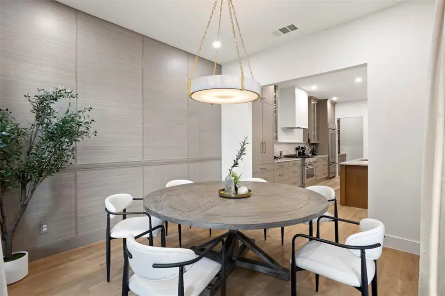 Dining area featuring a circular wood-finish table, a contemporary chandelier, textured wall paneling, and wood-finish flooring