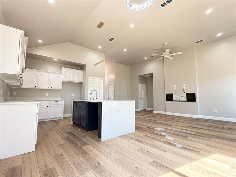 Kitchen with a kitchen island with sink, white cabinets, light wood-style floors, high vaulted ceiling, and open floor plan Kitchen with a kitchen island with sink, white cabinets, light wood-style floors, high vaulted ceiling, and open floor plan