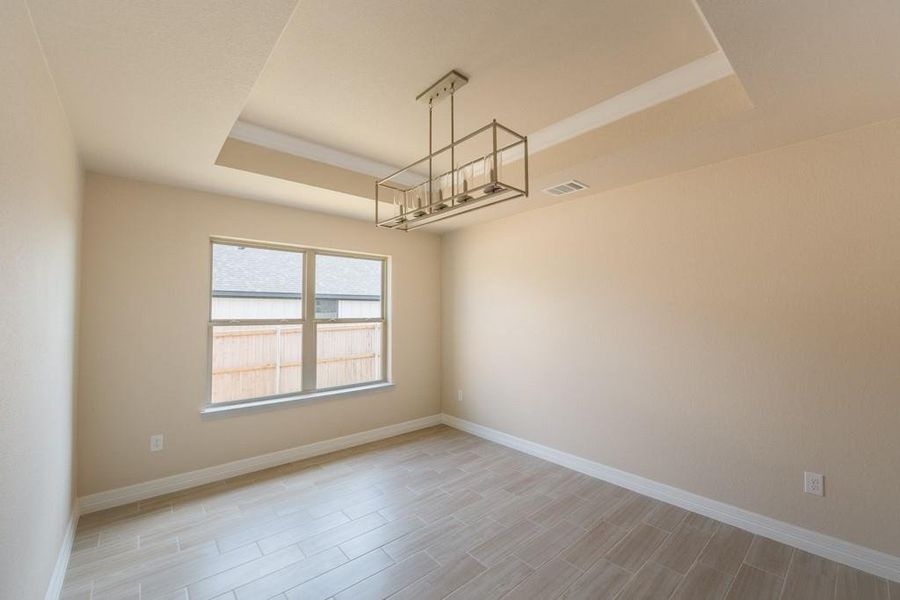 Unfurnished room featuring a tray ceiling, wood finish floors, and a chandelier Unfurnished room featuring a tray ceiling, wood finish floors, and a chandelier