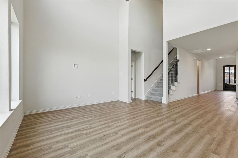 Unfurnished living room featuring light wood-style flooring, stairway, and a high ceiling