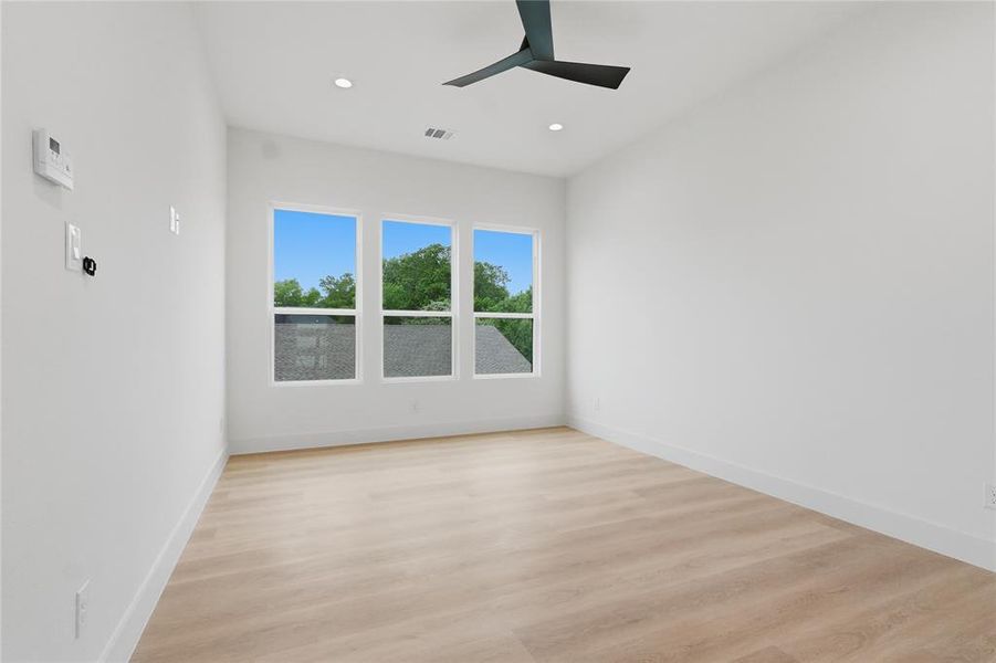 Bright room featuring three large windows, wood-finish flooring, recessed lighting, a ceiling fan, and white baseboards Bright room featuring three large windows, wood-finish flooring, recessed lighting, a ceiling fan, and white baseboards