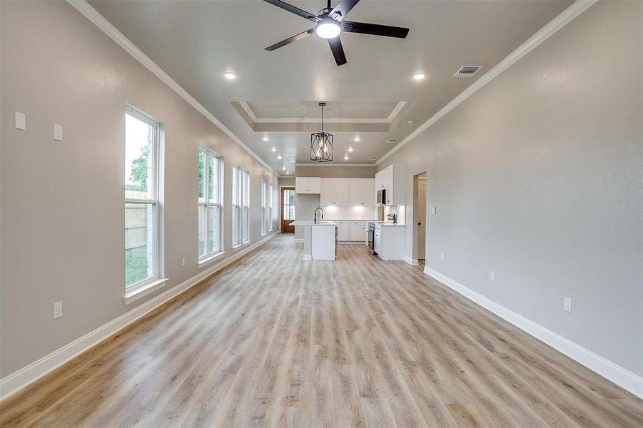 Unfurnished living room with crown molding, baseboards, light wood finished floors, and visible vents Unfurnished living room with crown molding, baseboards, light wood finished floors, and visible vents