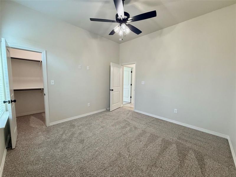 Unfurnished bedroom with light carpet, a walk in closet, ceiling fan, and a closet
