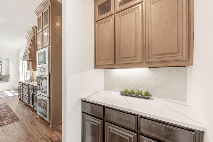 Kitchen with tan wood upper cabinets, white quartz countertop, herringbone tile backsplash, and built-in double oven wall unit.