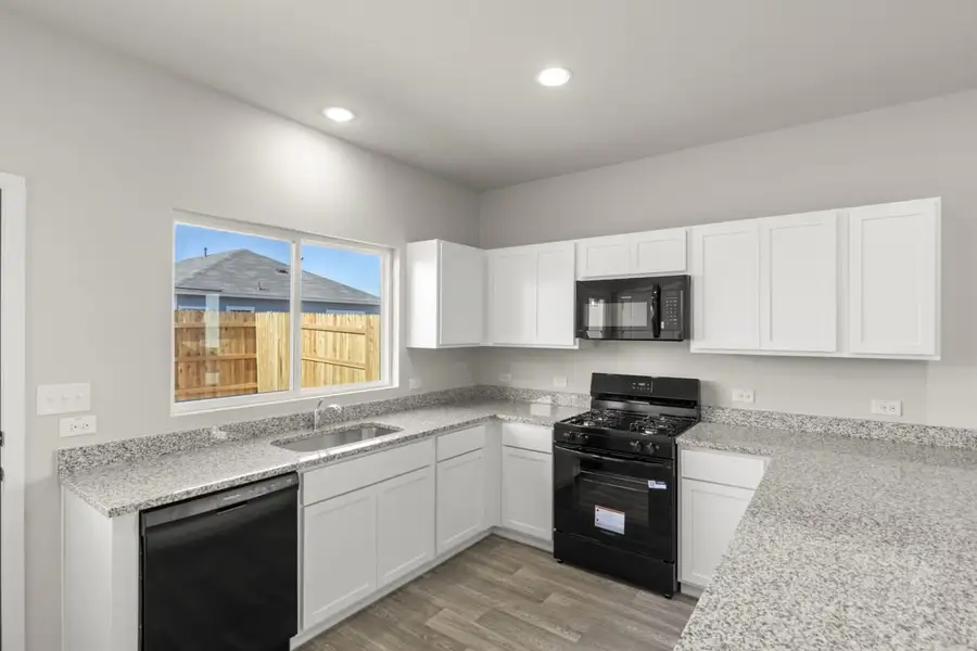 Image of a U-shaped kitchen with white cabinets, black appliances, a window above the sink, and white trim Image of a U-shaped kitchen with white cabinets, black appliances, a window above the sink, and white trim