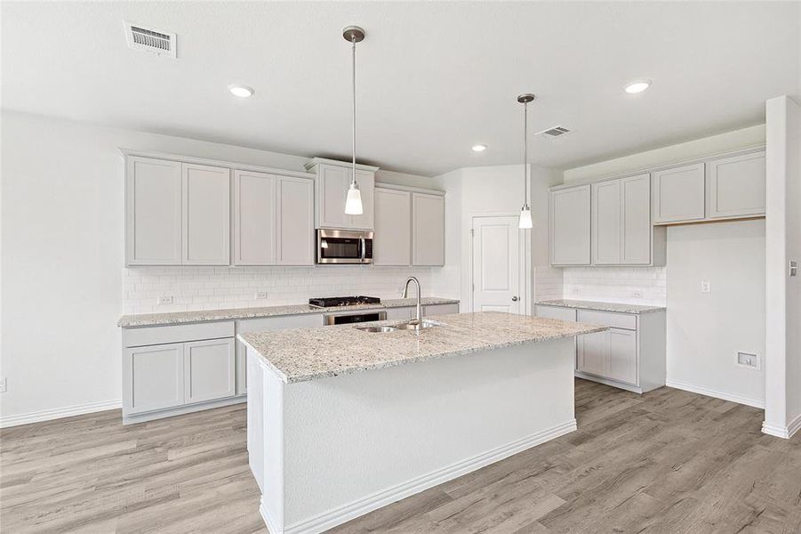 Kitchen with light hardwood / wood-style flooring, an island with sink, backsplash, hanging light fixtures, and sink