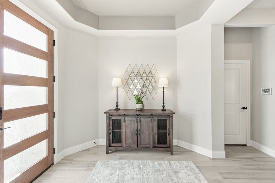 Entryway with wood and glass front door, rustic console table, and tray ceiling with light wood floors