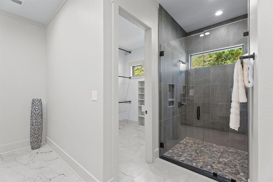 Bathroom featuring a walk in closet, light marble finish flooring, and a shower stall