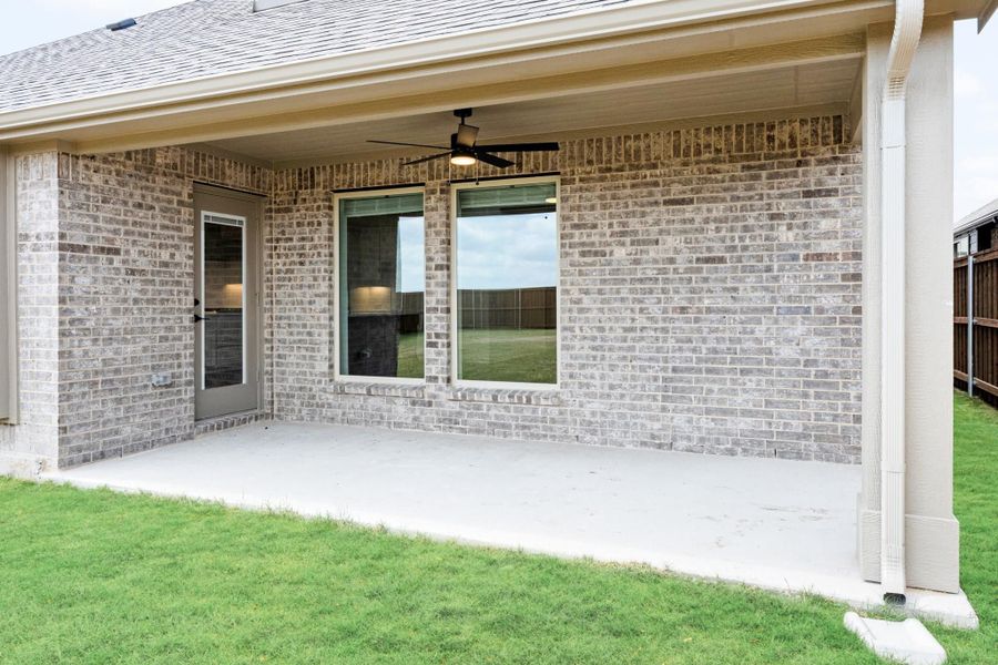 Covered back patio with ceiling fan, brick exterior, concrete floor, and green lawn