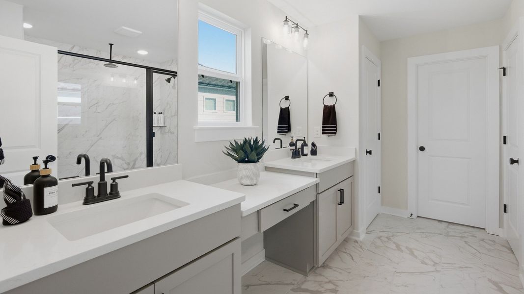 Connected primary bathroom with dual vanities paired with sizeable mirror