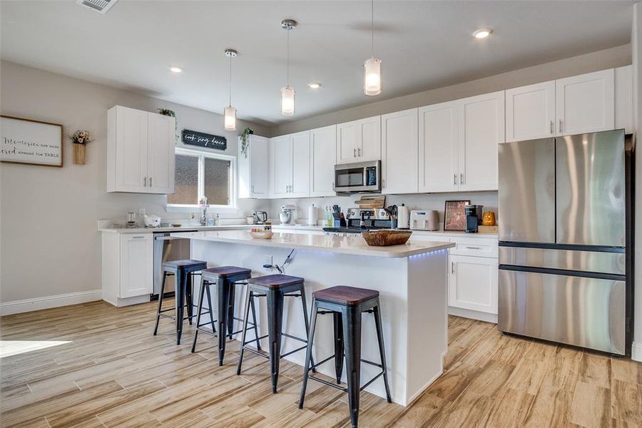 Kitchen with hanging light fixtures, stainless steel appliances, a breakfast bar area, white cabinets, and recessed lighting
