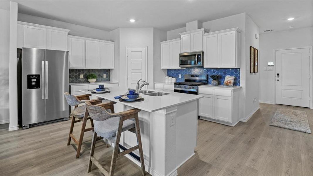 Kitchen with stainless steel appliances, white cabinetry, a breakfast bar, a center island with sink, and light wood-style floors