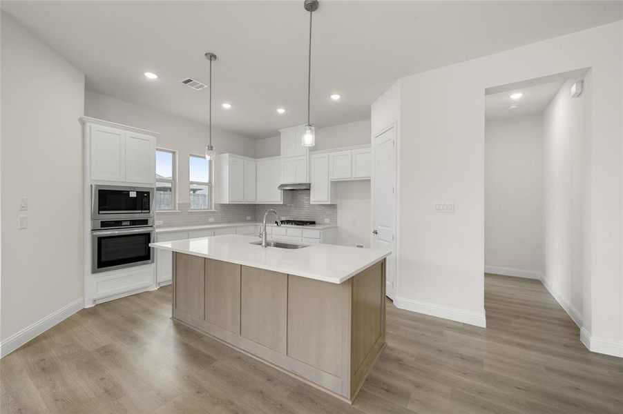 Kitchen with stainless steel oven, built in microwave, light countertops, backsplash, and light wood finished floors
