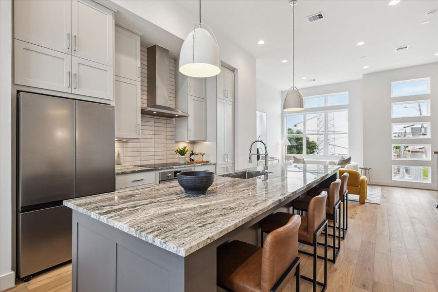 This modern kitchen features a spacious island with a marble countertop, stylish pendant lighting, and sleek stainless steel appliances. The open layout flows into a bright living area with large windows, offering plenty of natural light. Ideal for entertaining and family gatherings.